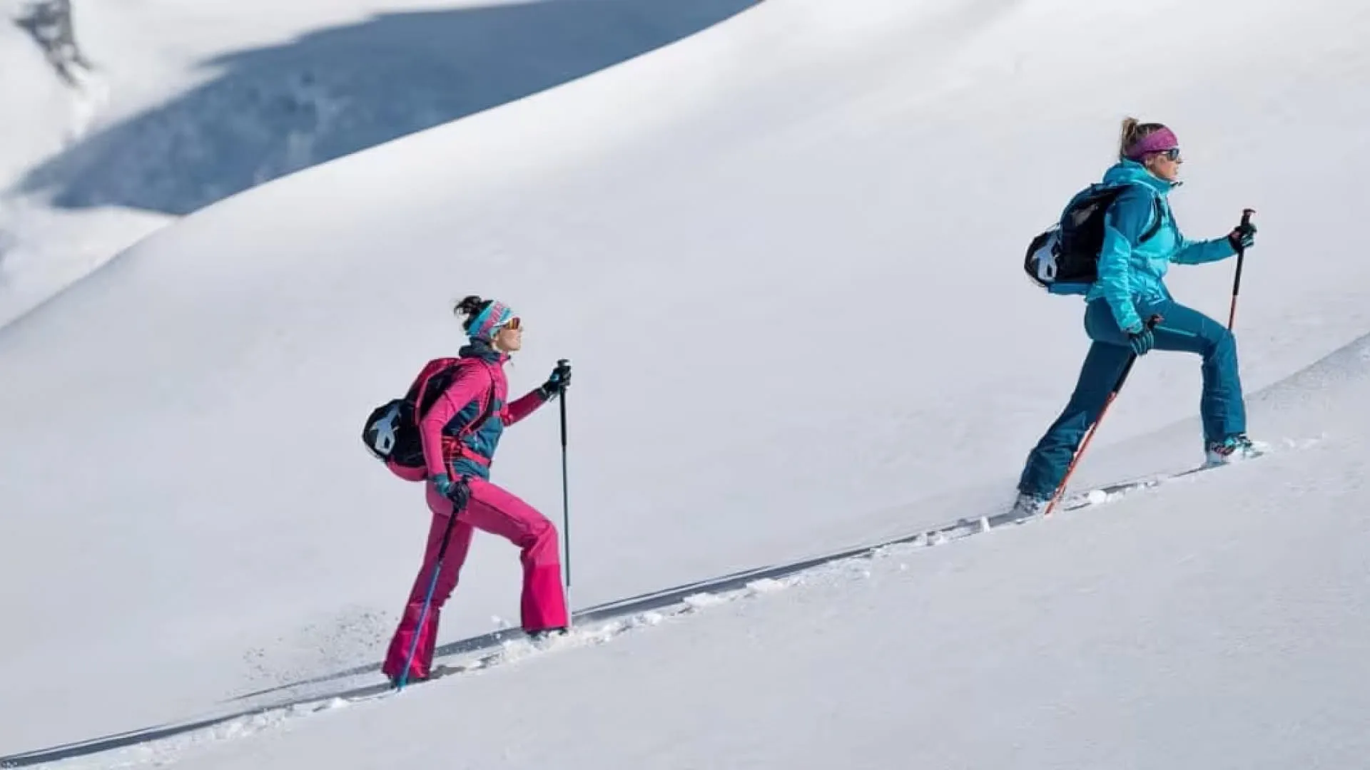 Drei Skitourengeherinnen im Schnee mit Bergen im Hintergrund.